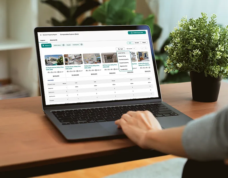Person using a laptop to compare property listings and prices on a real estate platform, with a green plant on the desk nearby.