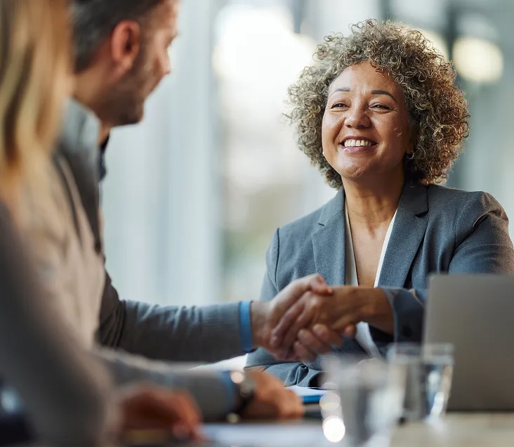 Professional woman smiling and shaking hands with a client during a business meeting in a modern office.