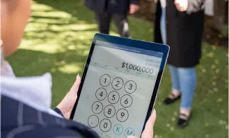 Real estate agent entering a $1,000,000 bid on a tablet during an outdoor property auction.