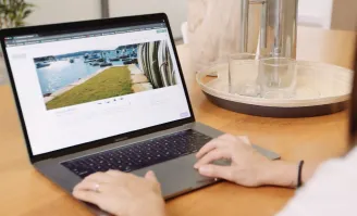 Person editing a waterfront property listing on a laptop, showing marina view and lawn area on screen.