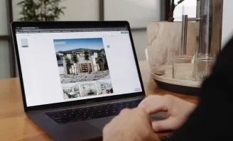 Person reviewing a property listing design on a laptop with real estate images displayed on screen.